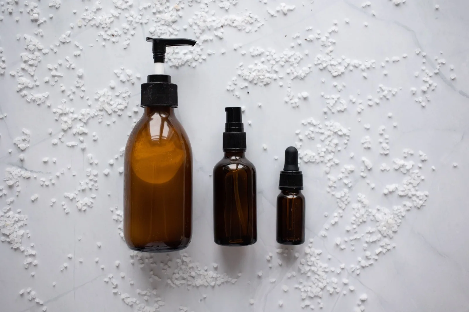 Amber glass pump, spray and dropper bottles on a marble surface, shown as packaging examples